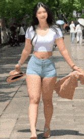 a woman in a white crop top and denim shorts is walking down the street .