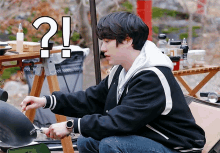 a man in a black jacket is cooking with a question mark above his head