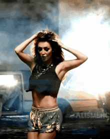 a woman in a crop top and shorts is standing in front of a car with the word alismeh on the bottom