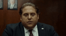 a man in a suit and tie is sitting at a table with his eyes closed and his hand on his face .