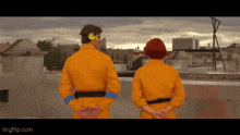 a man and a woman standing on a roof with their hands behind their backs