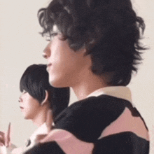 two young men are standing next to each other and one of them is wearing a black and pink striped shirt .