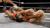 two women are wrestling in a wrestling ring and one of them is laying on the floor .