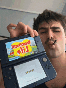 a man is smoking a cigarette while holding up a video game that says ' nintendo 3ds ' on it