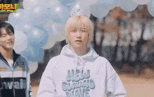 a man wearing a white hoodie and a crown is standing in front of balloons .
