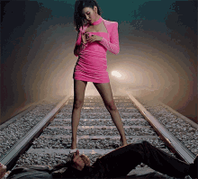 a woman in a pink dress is standing on train tracks looking at her phone