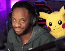 a man wearing headphones holds a stuffed pikachu on his lap