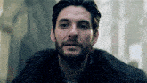 a man with a beard is wearing a black fur coat .