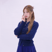 a woman wearing a blue sweater and a blue skirt is standing with her arms crossed