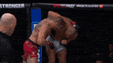 two men are wrestling in a cage with a referee in the background .