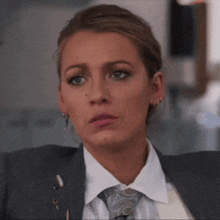 a woman wearing a suit and tie looks serious