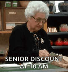 an elderly woman is sitting at a desk counting money with the words `` senior discount at 10 am '' above her .