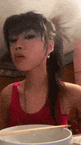 a woman in a red tank top is eating noodles with chopsticks .