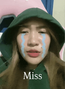 a woman with tears on her face is wearing a green hoodie and the word miss is above her