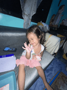 a little girl is sitting on a couch with her hand in the air