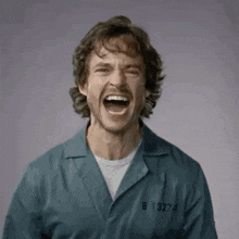 a man in a prison uniform is laughing with his mouth wide open and the number 8 on his jacket .