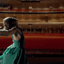 a woman in a green dress is dancing on a stage in an auditorium