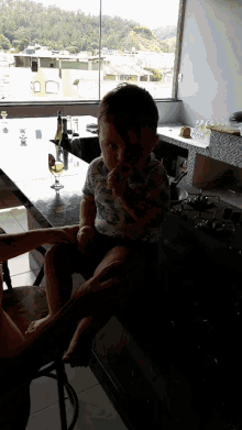 a baby is sitting on a chair in front of a window with a glass of wine