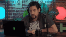 a man wearing headphones sits in front of a laptop with a razer logo on it