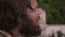 a man with a beard and long hair is smoking a cigarette in a close up of his face .