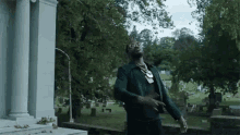 a man in a green jacket and sunglasses is standing in a cemetery .