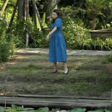 a woman in a blue dress is standing in a grassy area