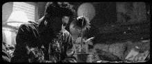 a black and white photo of a man looking at a potted plant