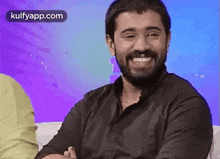 a man with a beard is sitting on a couch smiling .