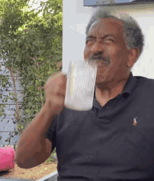 a man wearing a black polo shirt with a pony on it drinks from a glass