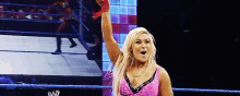 a woman in a pink dress is standing in a wrestling ring with her hand up .