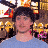 a man with curly hair and a mustache is standing in front of a crowd of people on a city street .