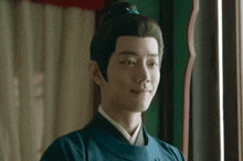 a man in a blue robe is smiling and looking out a window .