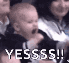 a baby is screaming in a crowd of people while a woman holds it .