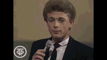 a man in a suit and tie is holding a microphone and talking into it .