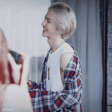 a man wearing a plaid shirt and a tank top smiles