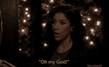 a woman is standing in front of a christmas tree and saying `` oh my god ! ''