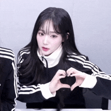 a girl wearing a black and white adidas jacket makes a heart shape with her hands