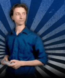 a man in a blue shirt holds a remote control in front of a blue and white striped background