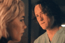 a man and a woman are looking at each other in a dark room . the man is wearing a scrub top .