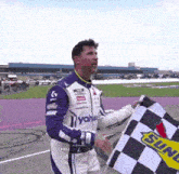 a man in a racing suit holds a checkered flag that says sunoco