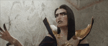 a woman with long black hair and a gold collar is standing in front of a white wall