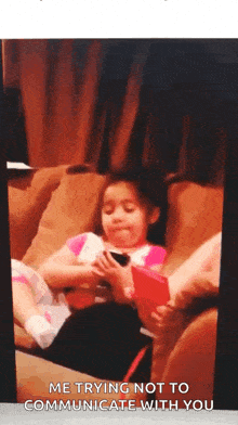 a little girl is sitting on a couch with a cell phone in her hand and says " me trying not to communicate with you "