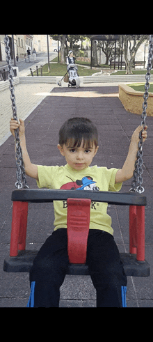 a young boy wearing a yellow shirt with snoopy on it sits on a swing in a park