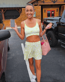 a woman in a crop top and shorts is holding a cell phone and a pink bag
