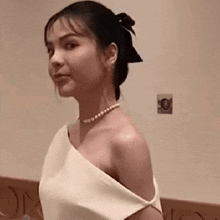 a woman in a white dress and pearls is standing in front of a wall .