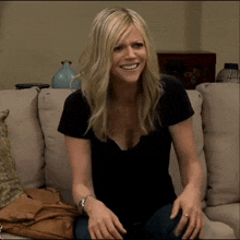 a woman in a black shirt is sitting on a couch and smiling