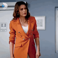 a woman in an orange jacket is standing in a room