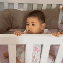 a baby is sitting in a crib looking over the railing