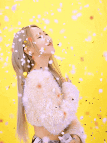 a woman in a white sweater is surrounded by confetti on a yellow background .