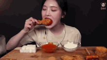 a woman is eating a piece of fried chicken with sauces on the table